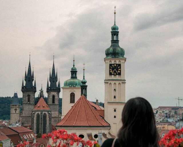 Kirchen Prag - Im Bildvordergrund steht eine Frau, welche sich eine Kirche im Bildhintergurnd anschaut.